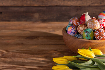 Many colorful Easter eggs arranged in a wooden bowl stand on the table.