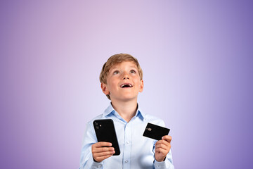 Kid with smartphone and credit card, happy portrait on empty purple background