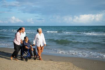 elderly asian woman sitting on wheelchair enjoying together time with friends walking on summer...