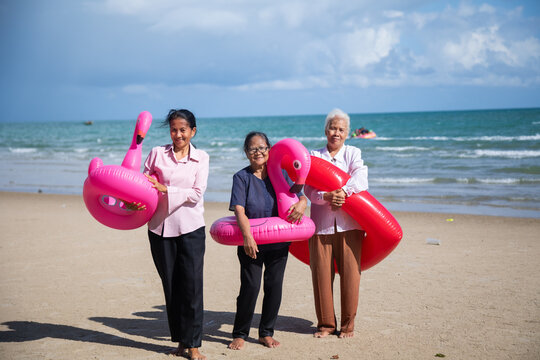 Portrait Asian senior women on beach. Happy retiredment life. Group of elderly Asian man and woman friends running with Bright inflatable ring to the beach.