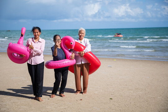 Portrait Asian senior women on beach. Happy retiredment life. Group of elderly Asian man and woman friends running with Bright inflatable ring to the beach.