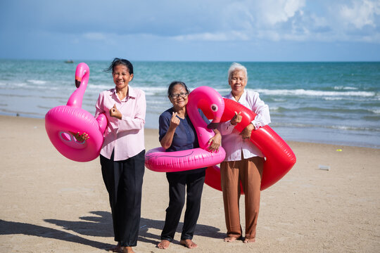 Portrait Asian senior women on beach. Happy retiredment life. Group of elderly Asian man and woman friends running with Bright inflatable ring to the beach.