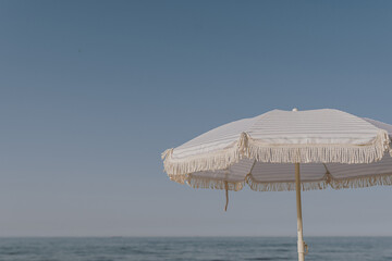 Minimal summer holidays vacation concept. Beach umbrella in front of blue sky and sea. Chilling, lounging on the beach