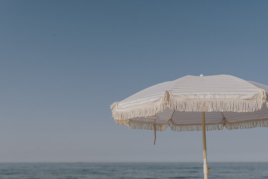 Minimal summer holidays vacation concept. Beach umbrella in front of blue sky and sea. Chilling, lounging on the beach - Powered by Adobe