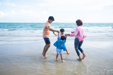 Happy holidays with family. Travel and vacations concept. Happy Asian young family mother father and two son walking together on the beach.