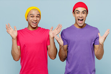 Young excited cheerful fun overjoyed couple two friends men wears casual clothes looking camera together spread hands look camera isolated on pastel plain light blue cyan background studio portrait