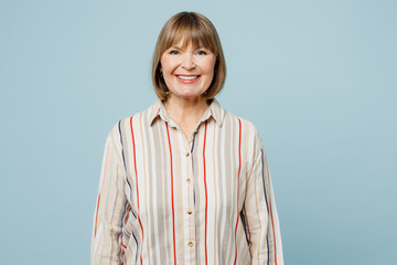 Elderly smiling cheerful fun happy cool optimist woman 50s years old wearing light striped shirt looking camera isolated on plain pastel blue cyan color background studio portrait. Lifestyle concept.