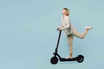 Full body side view healthy happy elderly woman 50s years old wearing shirt riding e-scooter raise up leg isolated on plain pastel light blue cyan color background studio portrait. Lifestyle concept. © ViDi Studio