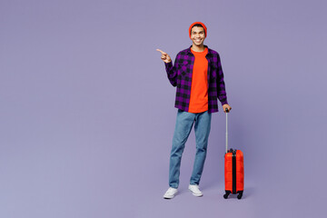 Full body traveler man wears casual clothes hold suitcase point aside isolated on plain purple color background Tourist travel abroad in free spare time rest getaway Air flight trip journey concept.