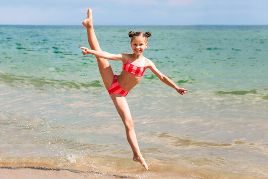Having fun Activity on Sea Coast. Happy Sea Children Holiday. Girl Child jumping in Splits on Sea Beach Background.  Sport and Recreation. 