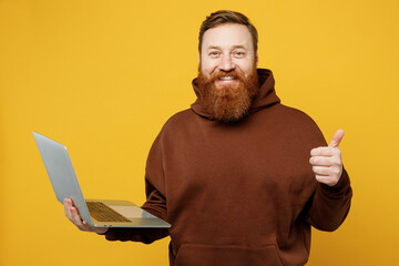 Side view smiling happy young redhead IT man wearing brown hoody casual clothes hold use work on...