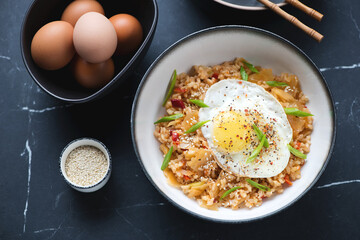 Bowl of kimchi fried rice topped with chicken egg, high angle view on a black marble background, horizontal shot