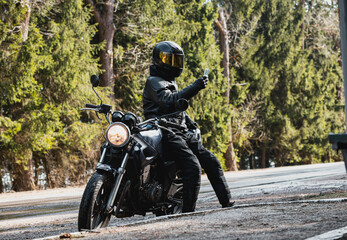 man in a leather motorcycle jacket with a motorcycle custom cafe racer in a helmet on a forest road...