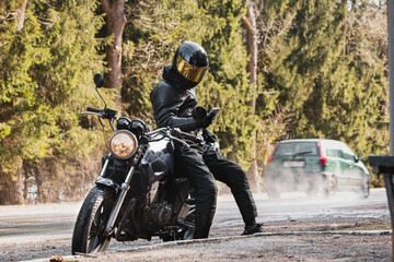 man in a leather motorcycle jacket with a motorcycle custom cafe racer in a helmet on a forest road...