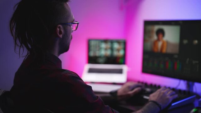 Young man in glasses working on video editing on computer doing montage and color correction. Professional man hand making edits on a special panel. Concept of creating video content.