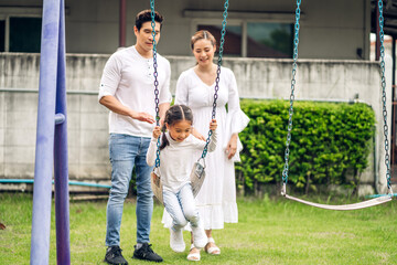 Portrait of enjoy happy love asian family father and mother with little asian girl smiling playing and pushing daughter on the swing moments good time at playground