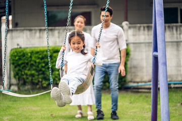 Portrait of enjoy happy love asian family father and mother with little asian girl smiling playing and pushing daughter on the swing moments good time at playground
