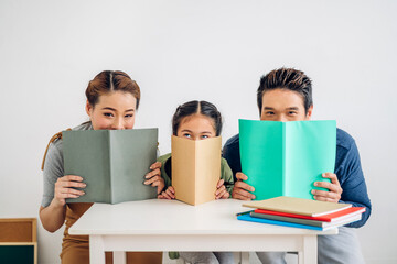 Portrait enjoy happy love asian family father and mother with little asian girl learn and study on table.Mom and dad with asian young girl hold book make homework in homeschool at home.Education
