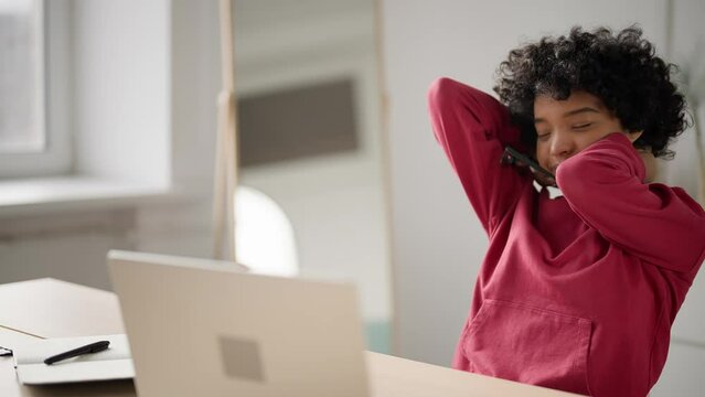 Tired business woman sits chair at table in home office doing warm up, stretches, massages neck in pain rubs tense muscles after long hard freelance work at computer laptop. Concept sedentary work.