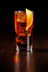 Cola with a slice of lemon and ice in a tall glass. Selective focus, black background.