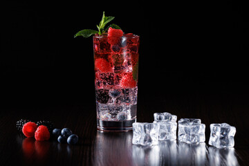 Iced carbonated drink with raspberries, blackberries and blueberries on a black background. Selective focus.