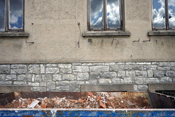 Container Mulde mit Bauschutt vor einem verfallenen Altbau mit Naturstein und Fassade in Beige und...