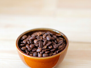 Fototapeta premium close-up of brown coffee beans in a bowl, coffee beans background, coffee beans in a bowl on wooden table, space for text, roasted coffee beans