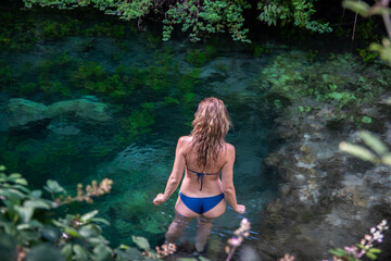 Beautiful girl on blue bikini standing in a river with cristal clear water.