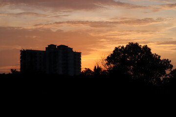 A sunset with a building in the distance can create a striking and picturesque scene, as the building's silhouette stands out against the colorful sky.