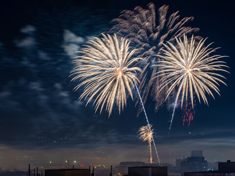 White fireworks burst in the midnight sky. Festive firework explosions over city celebrating holiday event. Pyrotechnic and firecracker concept. Long exposure night scene.