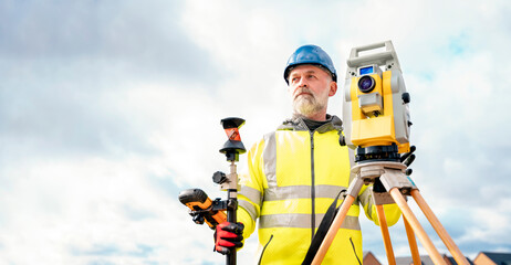 Surveyor builder site engineer with theodolite total station at construction site outdoors during...