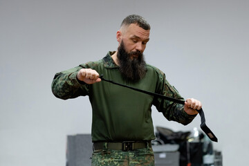 A bearded man in his 40s, a military medic demonstrates a combat medical tourniquet to stop blood during first aid