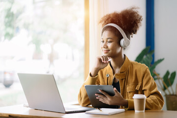 Smiling girl african relaxing at home, she is playing music using smartphone tablet, laptop, and wearing white headphones.