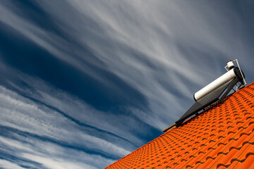 Solar water heater boiler on rooftop, dark blue sky with white washed clouds, space for text.