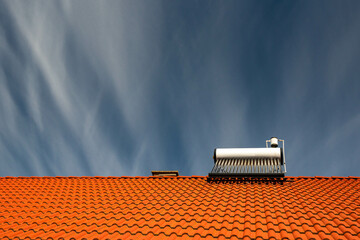 Front view of a solar water heater boiler on rooftop, dark blue sky with white washed clouds, space for text.