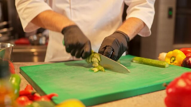 Close-up view of professional skillful male chef's hands chopping cucumber on cutting board. Hard-working experienced caucasian cook preparing ingredients before cooking delicious food.