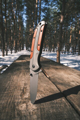 Folding knife is stuck into table top table standing in winter pine forest.