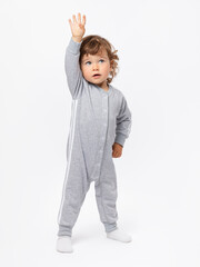 Gymnastics, fitness, exercise. A 1-2-year-old child goes in for sports in a gray jumpsuit, pulls his hand up on a white background.