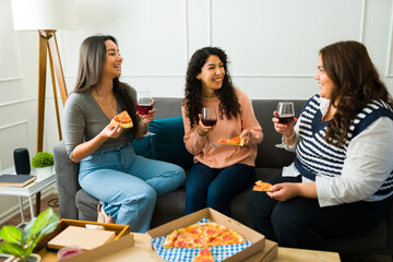 Happy female friends talking and eating pizza together