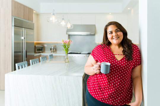 Beautiful hispanic woman in a luxury kitchen drinking coffee
