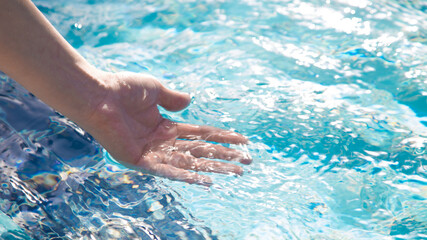Hand in the clear blue water of the pool in an expensive hotel.