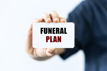 Funeral plan text on blank business card being held by a woman's hand with blurred background. Business concept and legal concept about funeral plan.