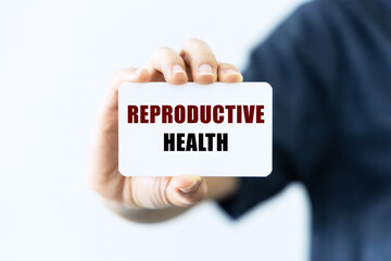 Reproductive health text on blank business card being held by a woman's hand with blurred background. Business concept about reproductive health.
