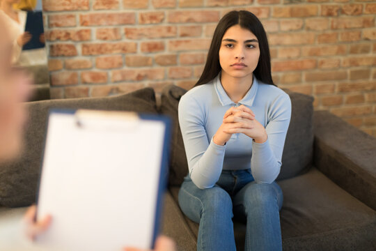 Depressed teen girl visiting psychologist helping to cope with problems awkward age sitting on sofa and listening doctor