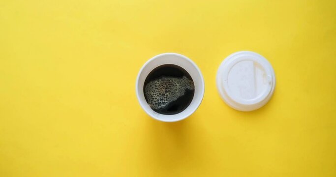 Craft paper coffee cup fills with drink. Coffee to go in a cup with a white lid on a yellow background. Looped 4K stop motion animation