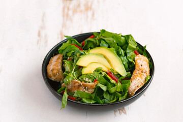 Healthy  vegetable buddha bowl salad with fried chicken and avocado, peppers and leaf lettuce on a white plate.