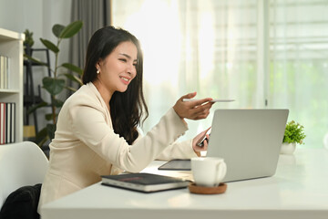 Smiling businesswoman checking marketing research results or statistics data on laptop at her office desk