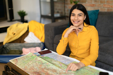 Happy young lady sitting with map and planning vacation, choosing new country for travel destination, smiling at camera