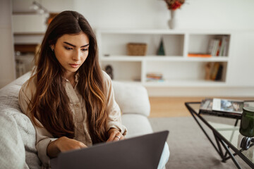 Busy serious millennial mixed race lady typing on laptop in living room interior, close up