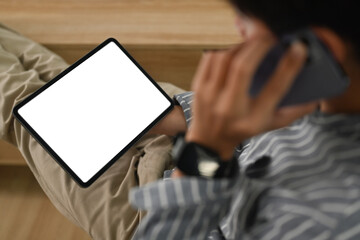 Above view of young businessman having phone conversation and checking information on digital tablet